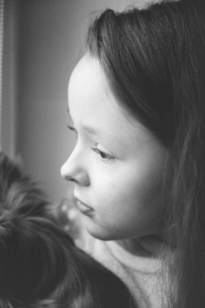 High contrast black and white image of a preschool age girl looking off into the distance in a country field while holding her stuffed animal toy.