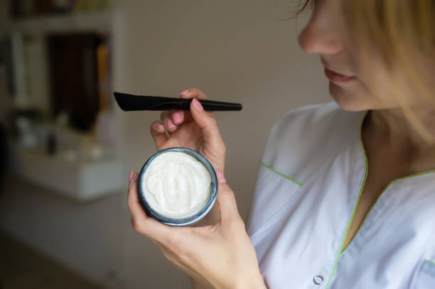 istock Cosmetologist's hand holding peeling cream in small box. Closeup. 1202531881