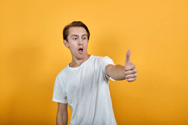 istock surprised young man in a white t-shirt thumb up lifestyle. 1202532130