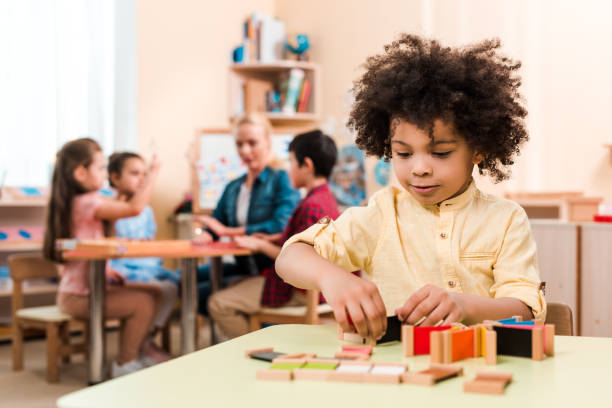 Selective focus of african american kid playing educational game with teacher and children at background in montessori school Selective focus of african american kid playing educational game with teacher and children at background in montessori school montessori education stock pictures, royalty-free photos & images