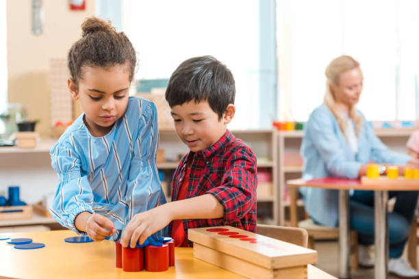 Selective focus of kids folding educational game with teacher at background in montessori class Selective focus of kids folding educational game with teacher at background in montessori class montessori education photos stock pictures, royalty-free photos & images