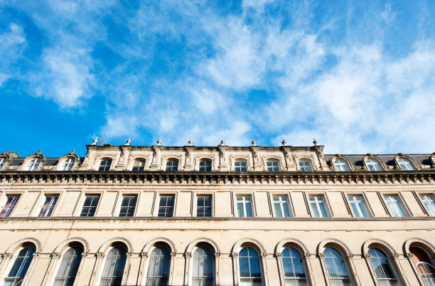 Sunlight in a cloudy blue sky frames the symmetrical angles of the towering Georgian sculptured architectural facade on this low angle view of this block of terraced houses or office accommodation building in Clifton, Bristol, England, UK