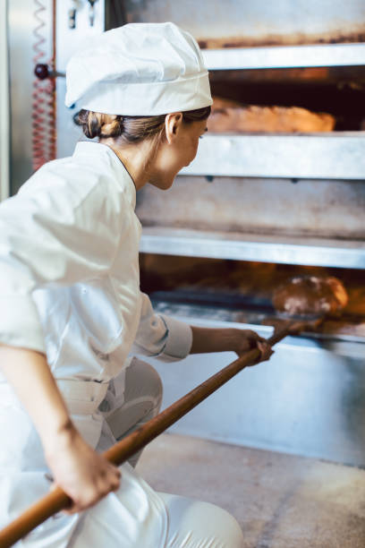 Baker putting bread in the bakery oven cowering on the floor of the bakery