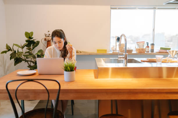 istock Young woman using laptop while having breakfast at home 1202535492