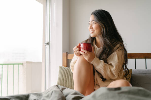 朝、ベッドで熱い飲み物を飲む美しい若い女性 - 温かい飲み物 ストックフォトと画像