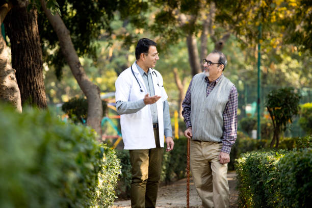Doctor talking with senior man in hospital garden Friendly doctor taking care of senior man in the hospital garden indian man walking in park stock pictures, royalty-free photos & images