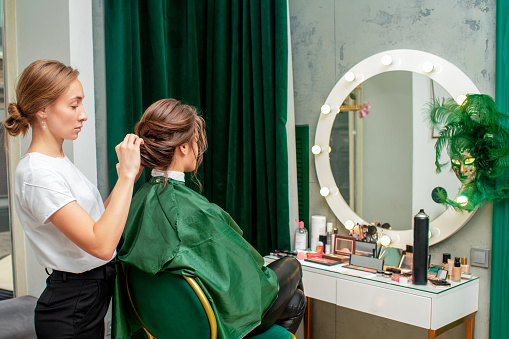 Hairdresser making hairstyle for young woman in beauty salon.
