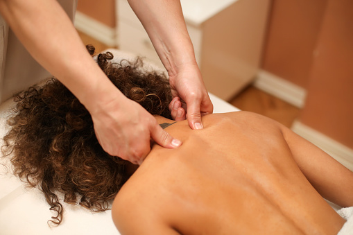 Young woman during a neck massage therapy. About 25 years old, Mixed race female.