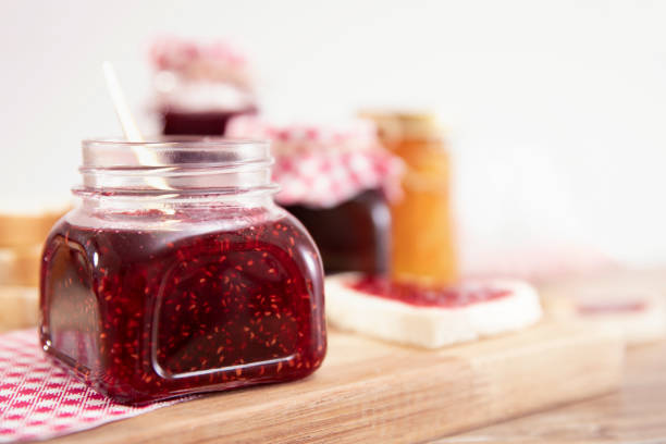 Slice of breads with jam in shape of heart, and raspberries over brown wooden table
