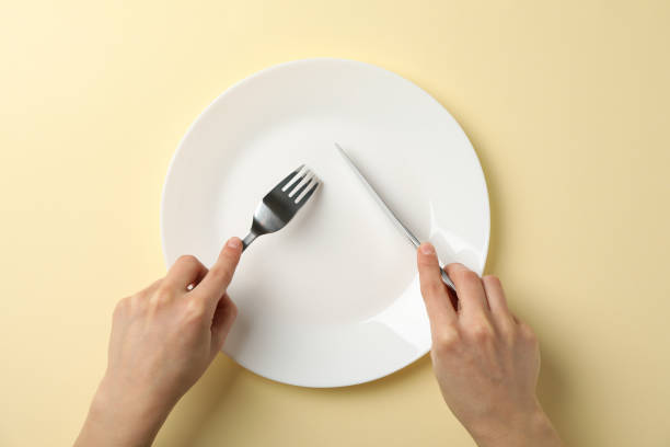 istock Female hands hold fork and knife on beige background with plate, top view 1202543231
