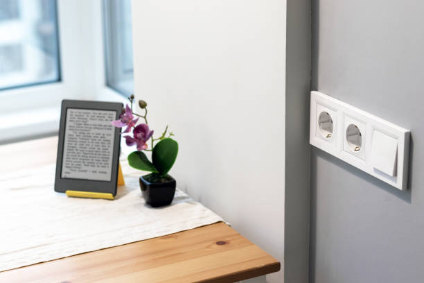 istock Group of white european electrical outlets and a switch located on a gray wall in a light modern kitchen with flower and e-book on the table by the window. Selective focus 1202545368