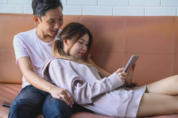 istock Happy Young Asian couple using digital tablet together on a sofa 1202545533