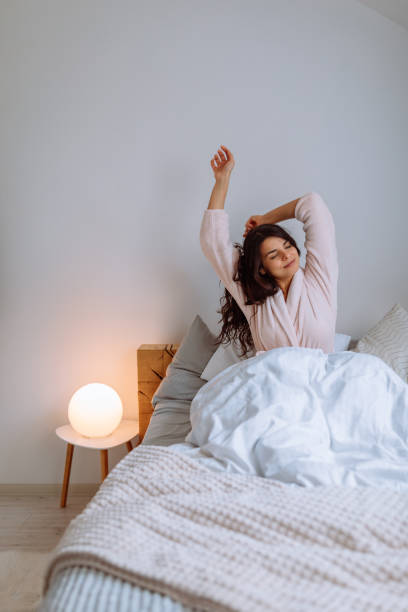 Greeting the new day with open arms Young woman waking up after a good night's sleep in her bed person waking up stock pictures, royalty-free photos & images