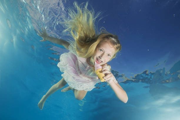 Girl in white dress eating ice cream underwater. Young beautiful girl poses underwater in the pool. Girl in white dress eating ice cream underwater. Young beautiful girl poses underwater in the pool. life stile stock pictures, royalty-free photos & images