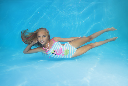 Young beautiful girl in a swimsuit is lying on the bottom of the pool