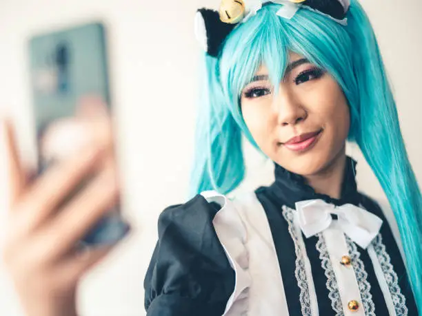 Millennial Asian woman of Taiwanese decent dressed in cosplay anime character. She is using her mobile phone. Selfie time!