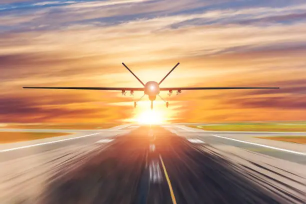 Photo of Military unmanned aerial vehicle takes off from runway at a military base in the evening at sunset.