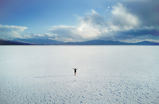 A scenic view from above on a lone woman standing in the middle of the salt desert in Salta, Argentina.