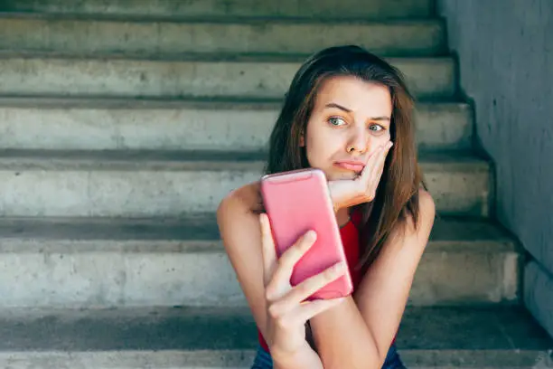 Displeased teen girl looking at her smartphone sitting on the stairs outdoors