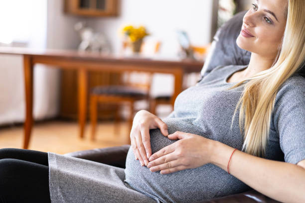 istock Pregnant woman sitting on sofa and making heart shape 1202555802