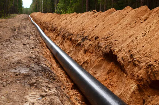 Photo of Natural gas pipeline construction work. A dug trench in the ground for the installation and installation of industrial gas and oil pipes.
