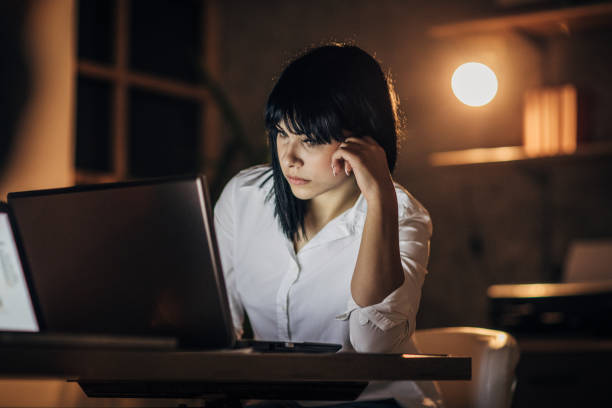 istock Young woman working late at night in office alone 1202558412