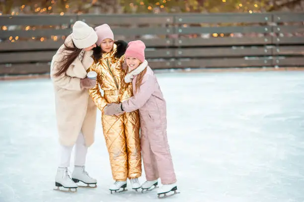 Little adorable girls with her mother skating on ice-rink. Family winter fun