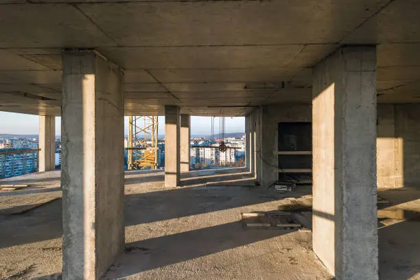 Photo of Interior of a concrete residential apartment building room with unfinished bare walls and support pillars for future walls under construction.