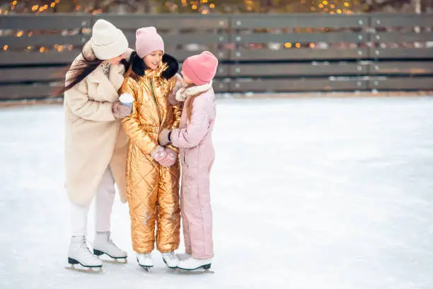 Little adorable girls with her mother skating on ice-rink. Family winter fun