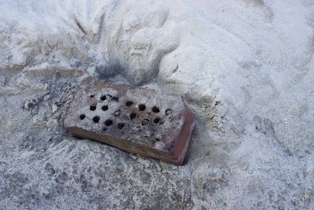 one old dirty brown brick lies on gray sand in the street