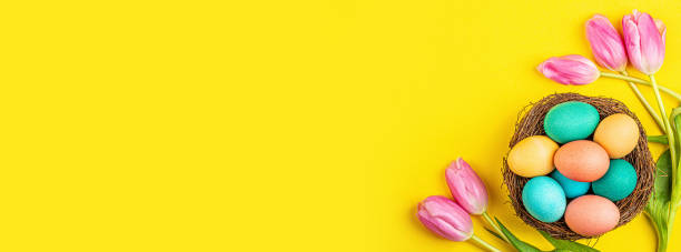 istock Stylish background with colorful easter eggs isolated on yellow background with pink tulip flowers. Flat lay, top view, mockup, overhead, template 1202565067