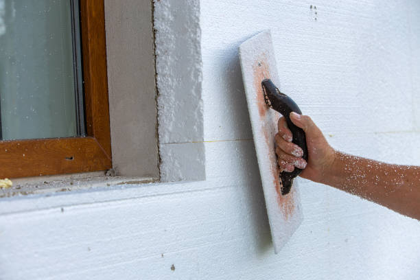 istock Hand of a worker with a tool for sanding and making smooth and even the surface of a house wall insulated with styrofoam insulation sheets. 1202566841