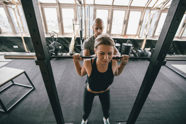 istock Woman exercise with barbell with her trainer 1202569575