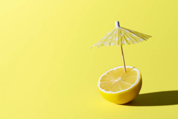 Lemon fruit and cocktail umbrella. Summer drink concept Lemon fruit and a cocktail umbrella stuck in it, on yellow background. Summer drink concept. Lemonade for summer heat. Ingredient for drink. drink umbrella stock pictures, royalty-free photos & images
