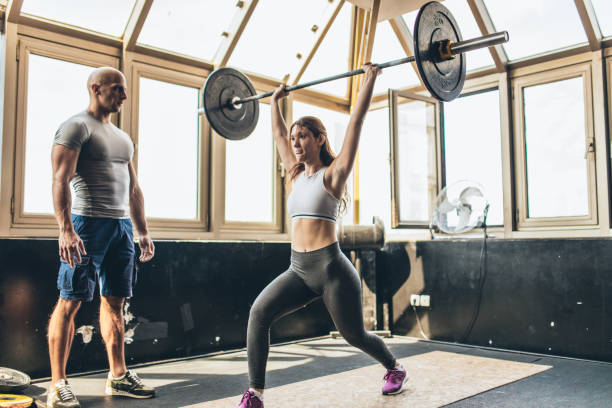 istock Woman exercise with barbell with her personal trainer 1202569893