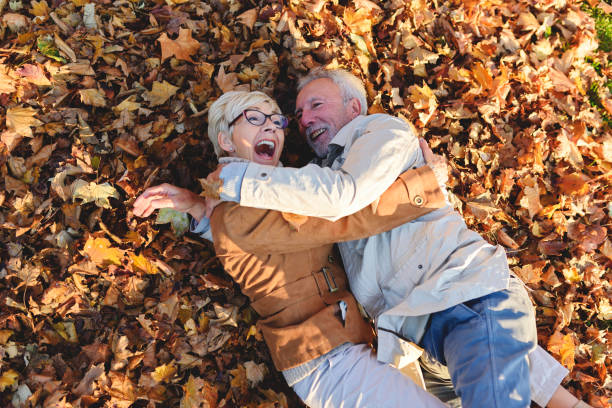 istock Cheerful active senior couple lying on ground rolling around in autumn leaves having fun 1202570121