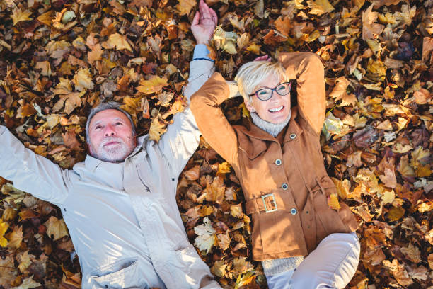 istock Cheerful active senior couple lying on ground rolling around in autumn leaves having fun 1202570188