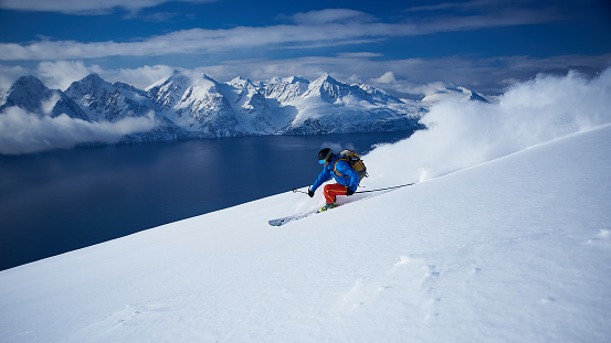Skier spraying powder snow with the fjord and the Lyngen alps in the background.