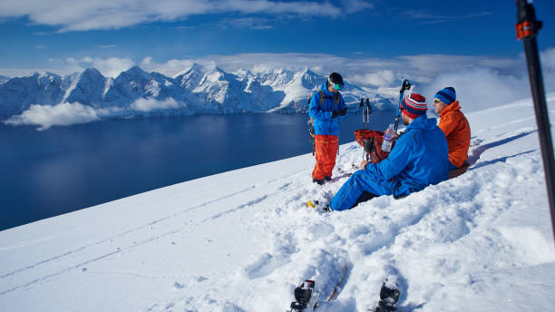 Ski touring lunch by the Lyngen fjord, Norway. Three men having a rest high on a snow covered mountain with the fjord and the Lyngen alps in the background. back country skiing photos stock pictures, royalty-free photos & images