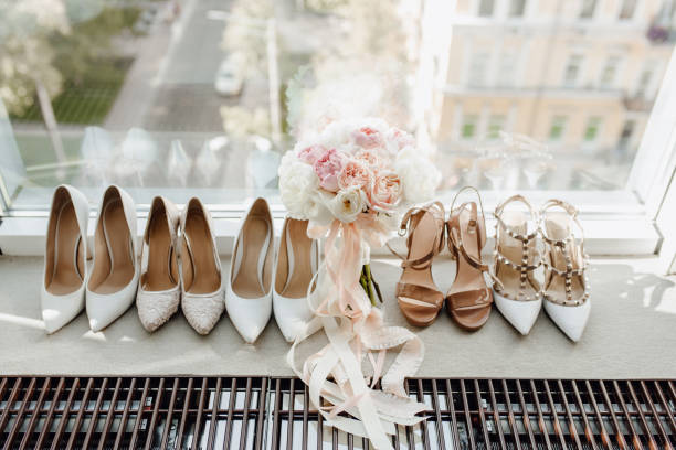 Woman Round-toe Pumps Shoes Collection and Bouquet Woman Round-toe Pumps Shoes Collection and Roses Flowers Bouquet Standing on Windowsill. Bridal Floral Accessory Decorated Ribbons, Spool Heels and Pointed Toe T-strap. City Street on Background wedding shoes stock pictures, royalty-free photos & images