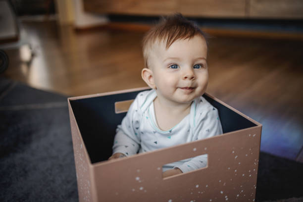 istock Curious little blond boy sitting in box and playing while looking at camera. Home interior. 1202591631