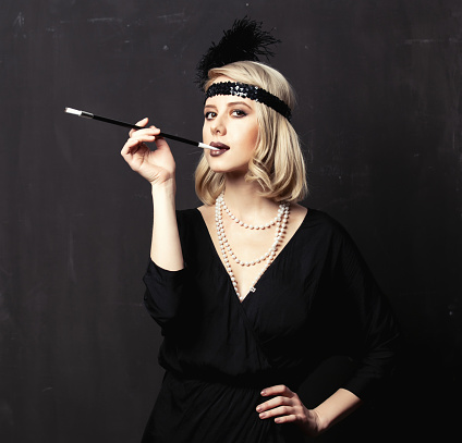 Beautiful blonde woman in twenties years clothes with smoking pipe on dark background