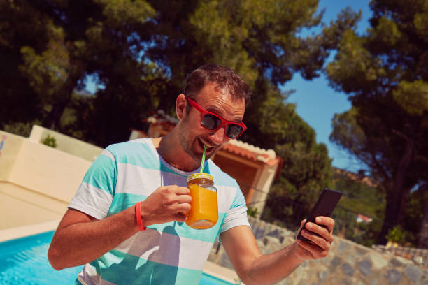 istock Attractive man using cellphone while drinking juice near swimming pool. 1202598131