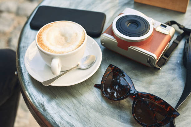 Cup of coffee with camera and cellphone on the table.