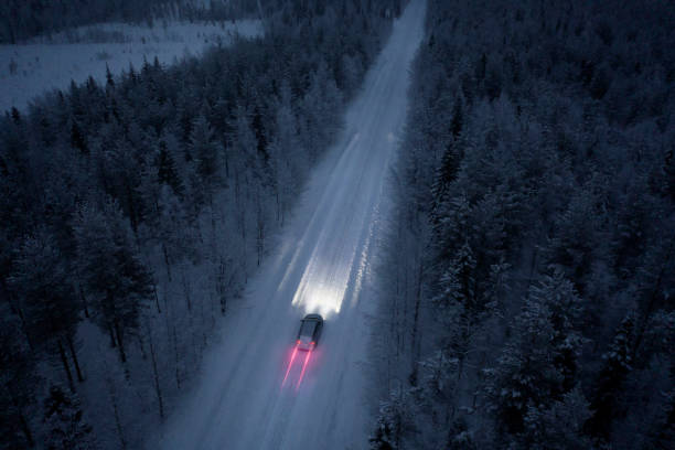 veduta aerea di una strada innevata che attraversa nella foresta innevata in finlandia - winterroad foto e immagini stock