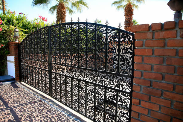 Palm Springs, California, USA- November 16,2010: Exterior view of black wrought iron security gate and brick wall. Intricate decorative pattern on gate.  Beautiful shadow of gate on driveway.