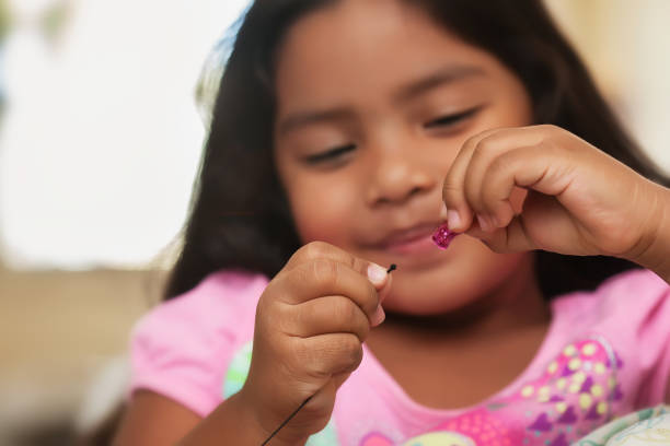 A cute little girl having fun while while creating bead jewelry using string and colorful beads. stock photo