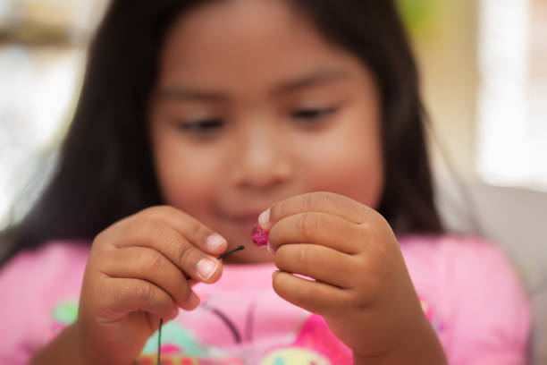 A child improving fine motor skills by using a pincer grip while holding string and beads. stock photo