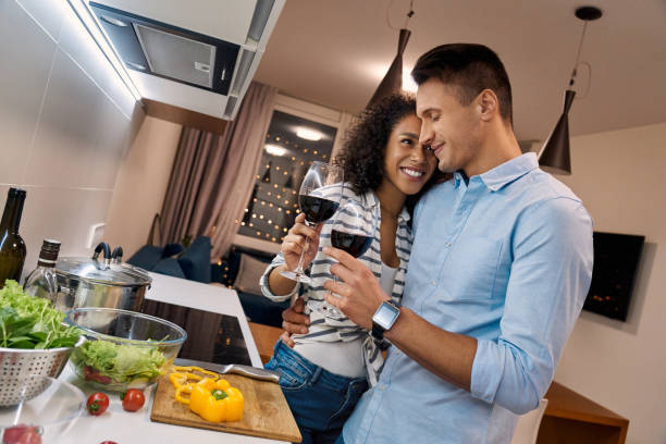 istock Romantic Date. Young multiethnic couple standing at kitchen cooking dinner hugging drinking wine smiling happy 1202612857