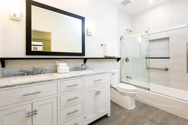 A contemporary modern bathroom design. featuring a bathtub with glass shower stall, toilet and his and her double sink vanity.